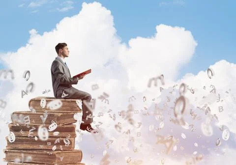 Man student on stack reading book and symbols flying around 库存照片