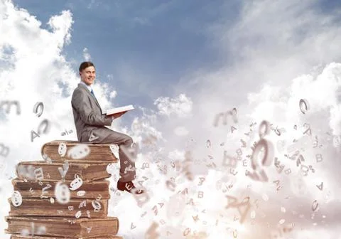 Man student on stack reading book and symbols flying around 库存照片