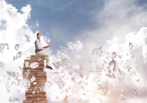 Man student on stack reading book and symbols flying around 스톡 사진