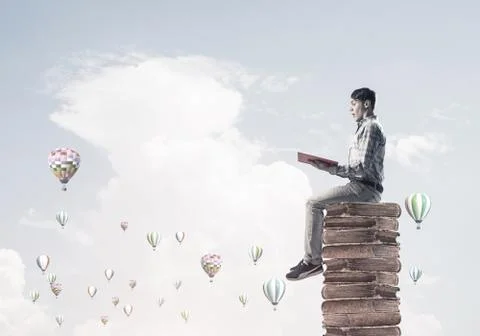 Man student on stack reading book and aerostats flying around 库存照片