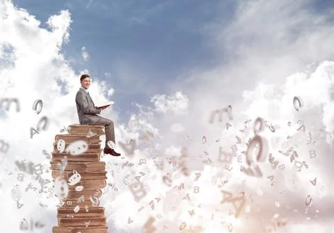 Man student on stack reading book and symbols flying around Foto stock