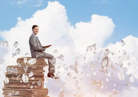 Man student on stack reading book and symbols flying around 库存照片