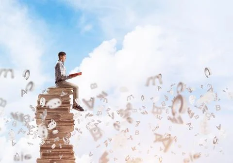 Man student on stack reading book and symbols flying around Foto stock