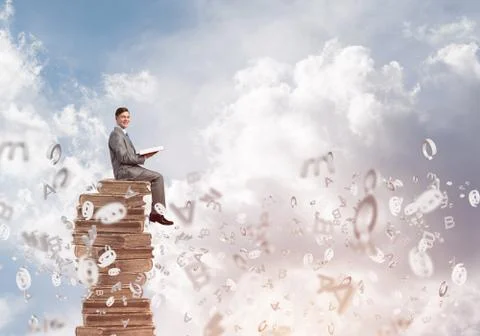 Man student on stack reading book and symbols flying around 库存照片