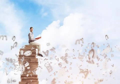 Man student on stack reading book and symbols flying around 库存照片