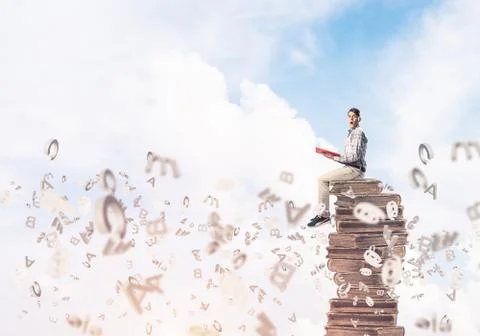 Man student on stack reading book and symbols flying around Foto stock