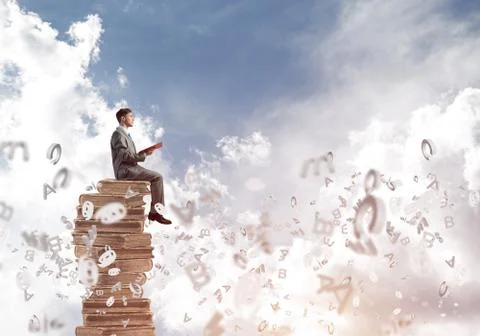 Man student on stack reading book and symbols flying around Foto stock