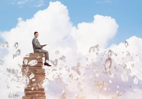 Man student on stack reading book and symbols flying around Foto stock