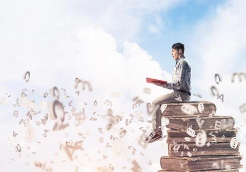 Man student on stack reading book and symbols flying around Foto stock