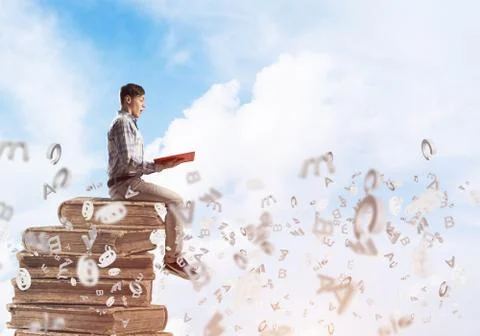 Man student on stack reading book and symbols flying around Foto stock