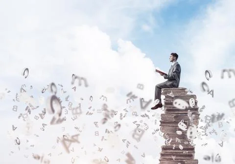 Man student on stack reading book and symbols flying around 스톡 사진