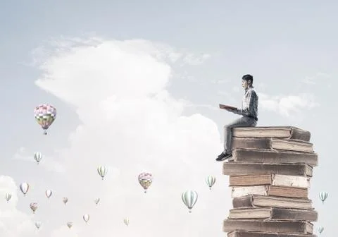 Man student on stack reading book and aerostats flying around 库存照片