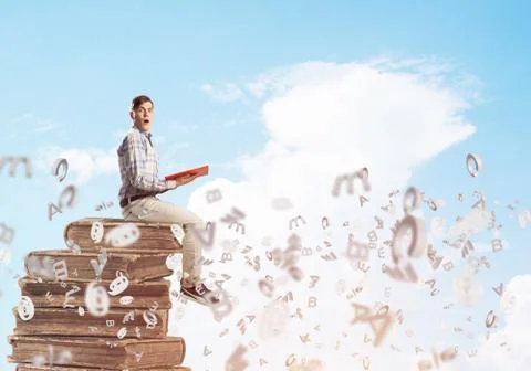 Man student on stack reading book and symbols flying around 库存照片
