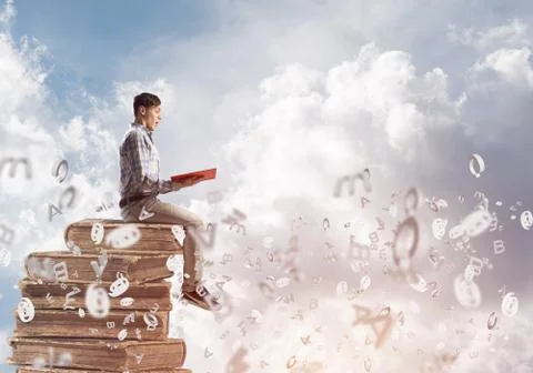 Man student on stack reading book and symbols flying around Foto stock