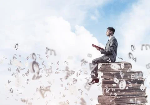 Man student on stack reading book and symbols flying around 库存照片