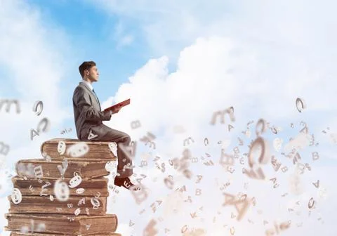 Man student on stack reading book and symbols flying around Foto stock