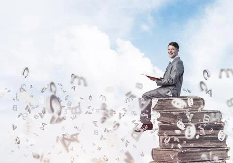 Man student on stack reading book and symbols flying around Foto stock