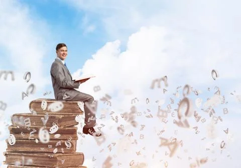 Man student on stack reading book and symbols flying around 库存照片