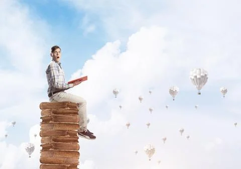 Man student on stack reading book and aerostats flying around 库存照片