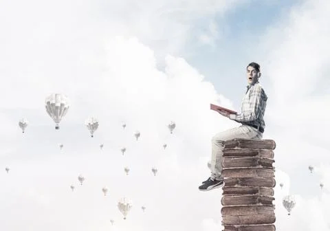 Man student on stack reading book and aerostats flying around 库存照片