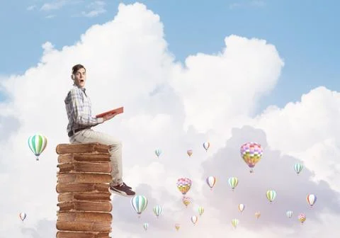 Man student on stack reading book and aerostats flying around 库存照片