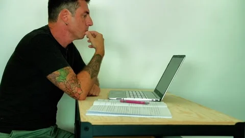 A man studies in front of a computer and a notebook while sitting at a desk Stock Footage 339774322