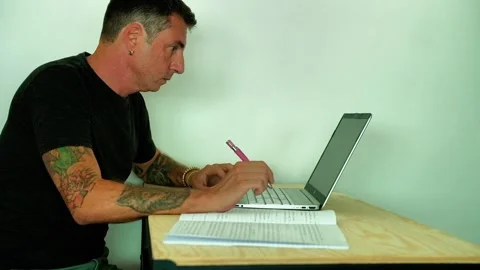 A man studies in front of a computer and a notebook while sitting at a desk Stock Footage 339774325