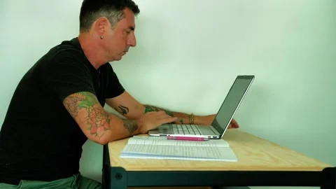 A man studies in front of a computer and a notebook while sitting at a desk Stock Footage 339774326