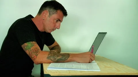 A man studies in front of a computer and a notebook while sitting at a desk Stock Footage 339774327