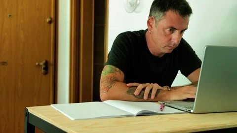 A man studies in front of a computer and a notebook while sitting at a desk Stock Footage 339774332
