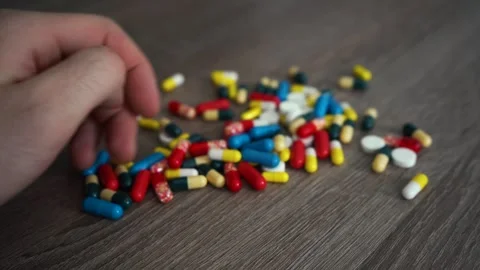 A man studies the multicolored pills lying in a handful on a wooden table Stockbeeldmateriaal 280380139