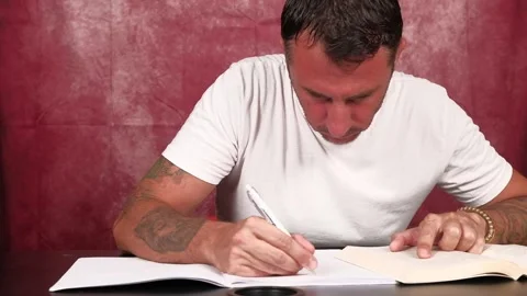 A man studies by reading from a book and writing notes in a notebook Stock Footage 341335543