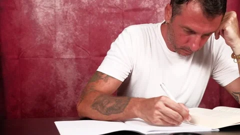 A man studies by reading from a book and writing notes in a notebook Stock Footage 341335727