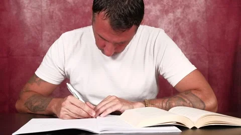 A man studies by reading from a book and writing notes in a notebook Stock Footage 341335827