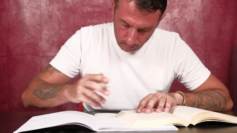 A man studies by reading from a book and writing notes in a notebook Stock Footage 341335925