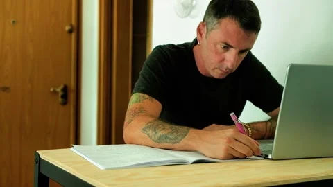 A man studies sitting at a desk and writing notes in a notebook Stock Footage 339774323