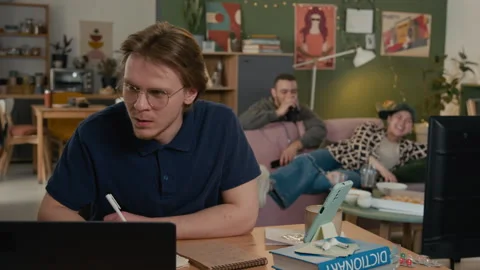 Man Studying at Desk with Distracting Roommates in Background Stock Footage 336622887