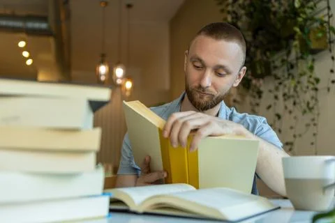 Man studying at a table with books and a cup of coffee while taking part in.. Stock Photos