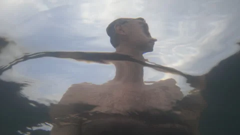 Man submerged in water looking up at the sky, enjoying a refreshing summer swim. Stock Footage 343110662