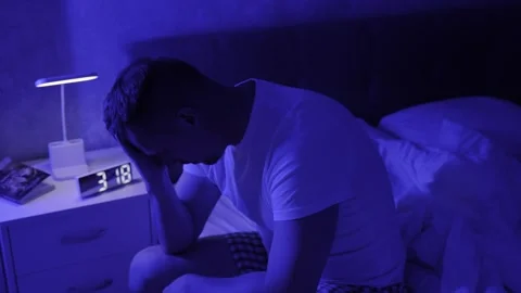 Man suffering from insomnia, sitting on bed near clock on bedside table. PT.. Stock Footage 290310403