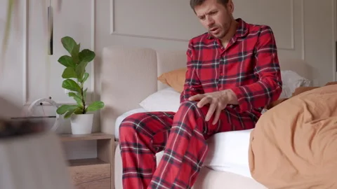 Man suffering from knee pain while trying to stand up from bed Stockbeeldmateriaal 335643463
