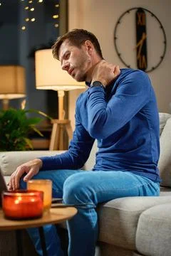 Man suffering from neck pain while sitting on sofa at home Stock Photos