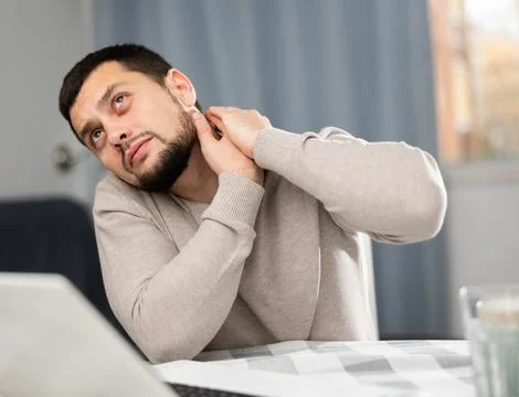 Man suffering from neck pain while sitting with laptop at home Stock Photos