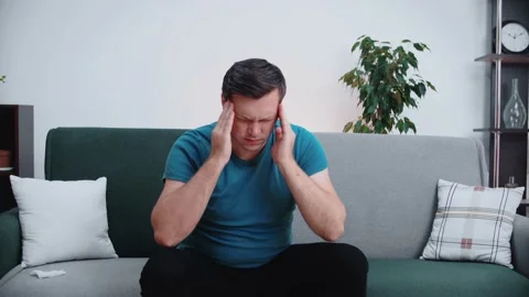 Man suffering from severe headache or migraine, sitting on sofa. Stock Footage 146364854