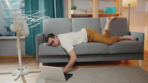 Man suffering sweating from heat is lying on the sofa under a cooling fan Stock Footage 225092058