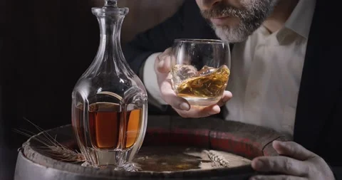 Man in a suit and beard (sommelier) takes a glass of whiskey on ice. Video stock 146333025