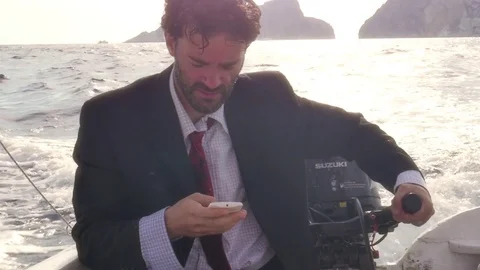 Man in suit with a briefcase texting on his smartphone while driving a boat in Stock Footage 78058943