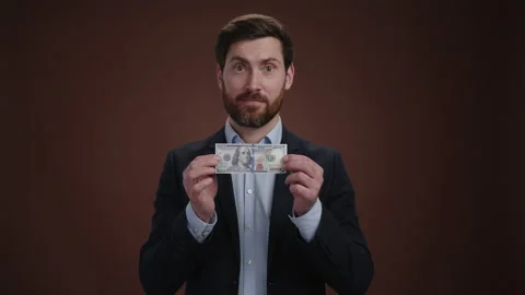 A man in a suit cracking a dollar bill while looking at the camera with a smile Stock Footage 236631489