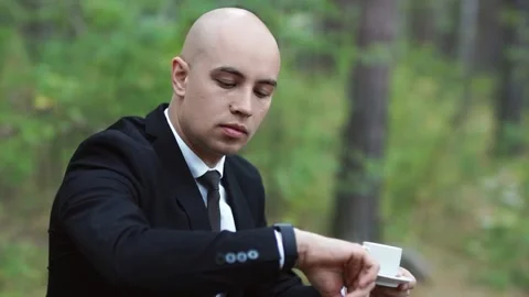 A man in a suit drinks coffee and looks at his wristwatch while sitting  Stock Footage 147329447