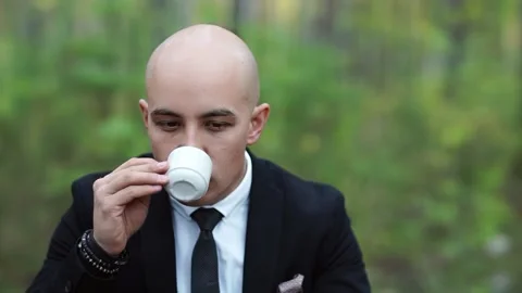 A man in a suit drinks coffee from a small cup and saucer in the park. Stock Footage 147329411
